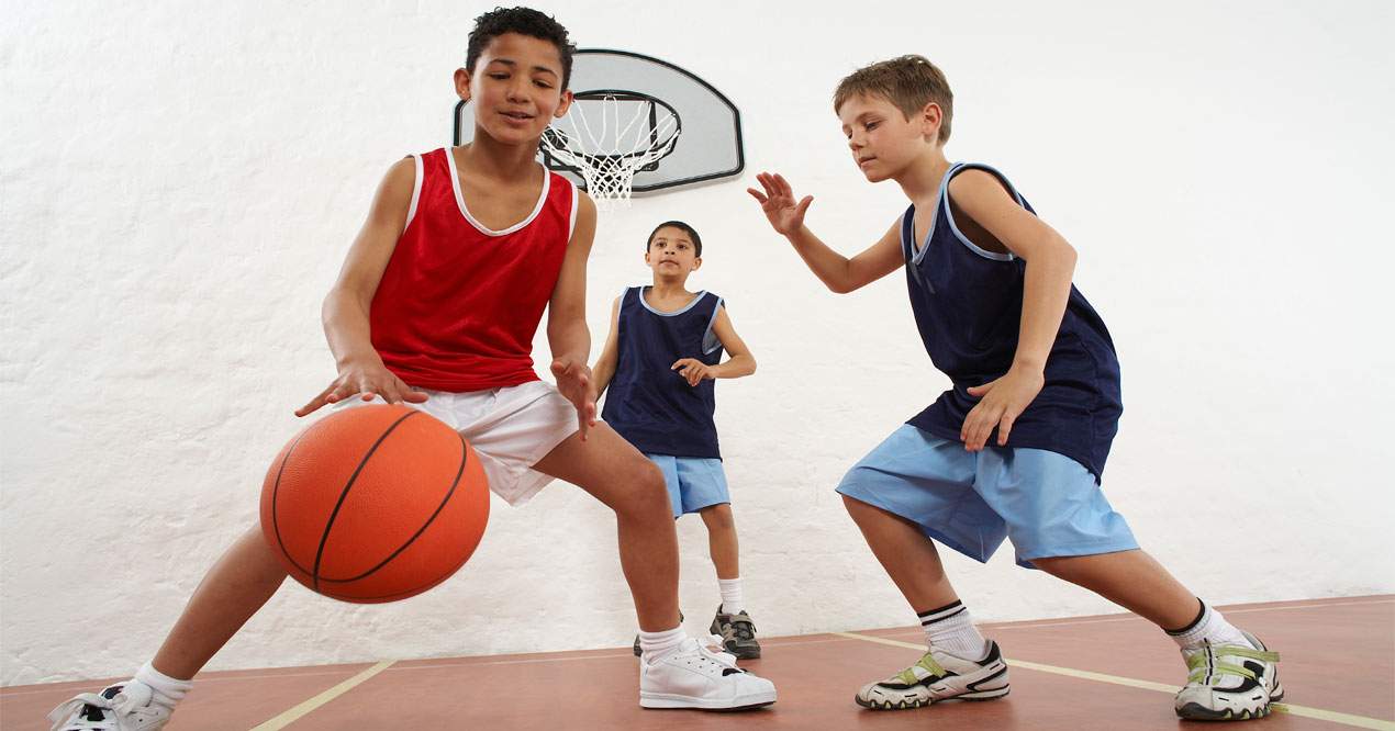 Tres niños jugando al baloncesto en su hora de actividades extraescolares.