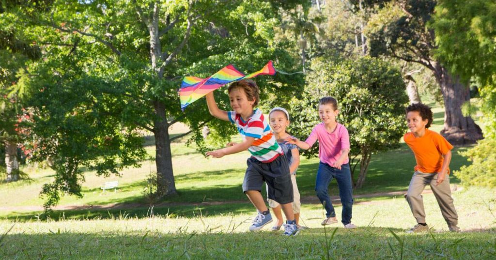 Niños corriendo por parque con una cometa.